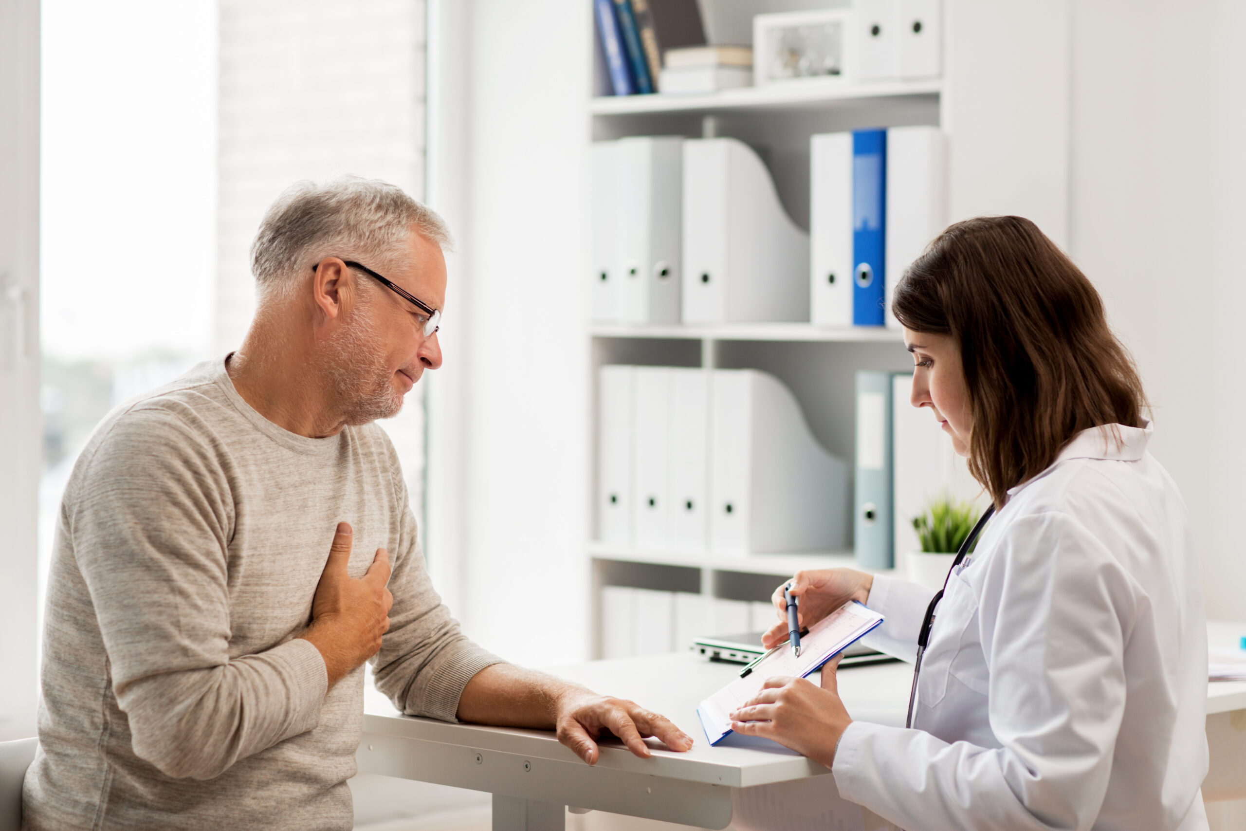 medicine, age, health care, cardiology and people concept - senior man and doctor with cardiogram on clipboard meeting in medical office at hospital